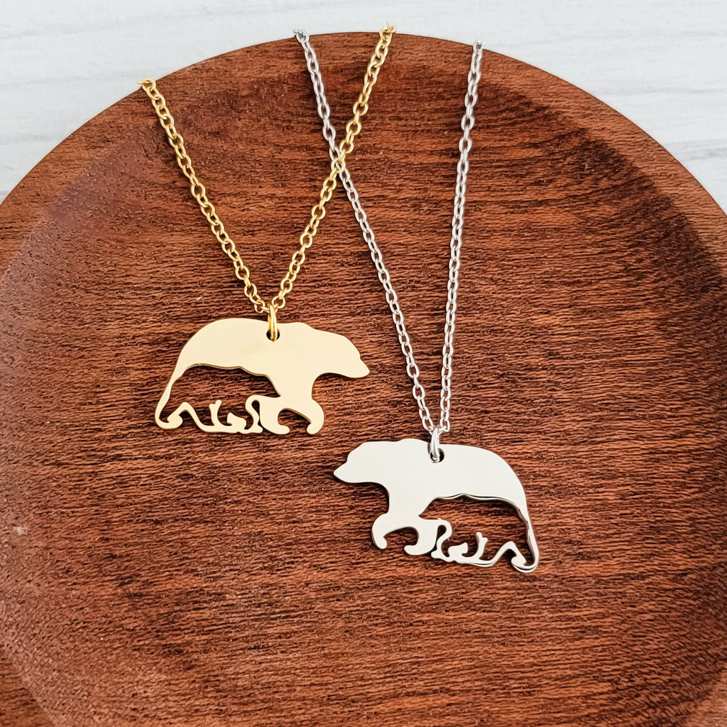 Roco Engraving gold and silver bear-and-cub pendant necklaces on a wooden plate