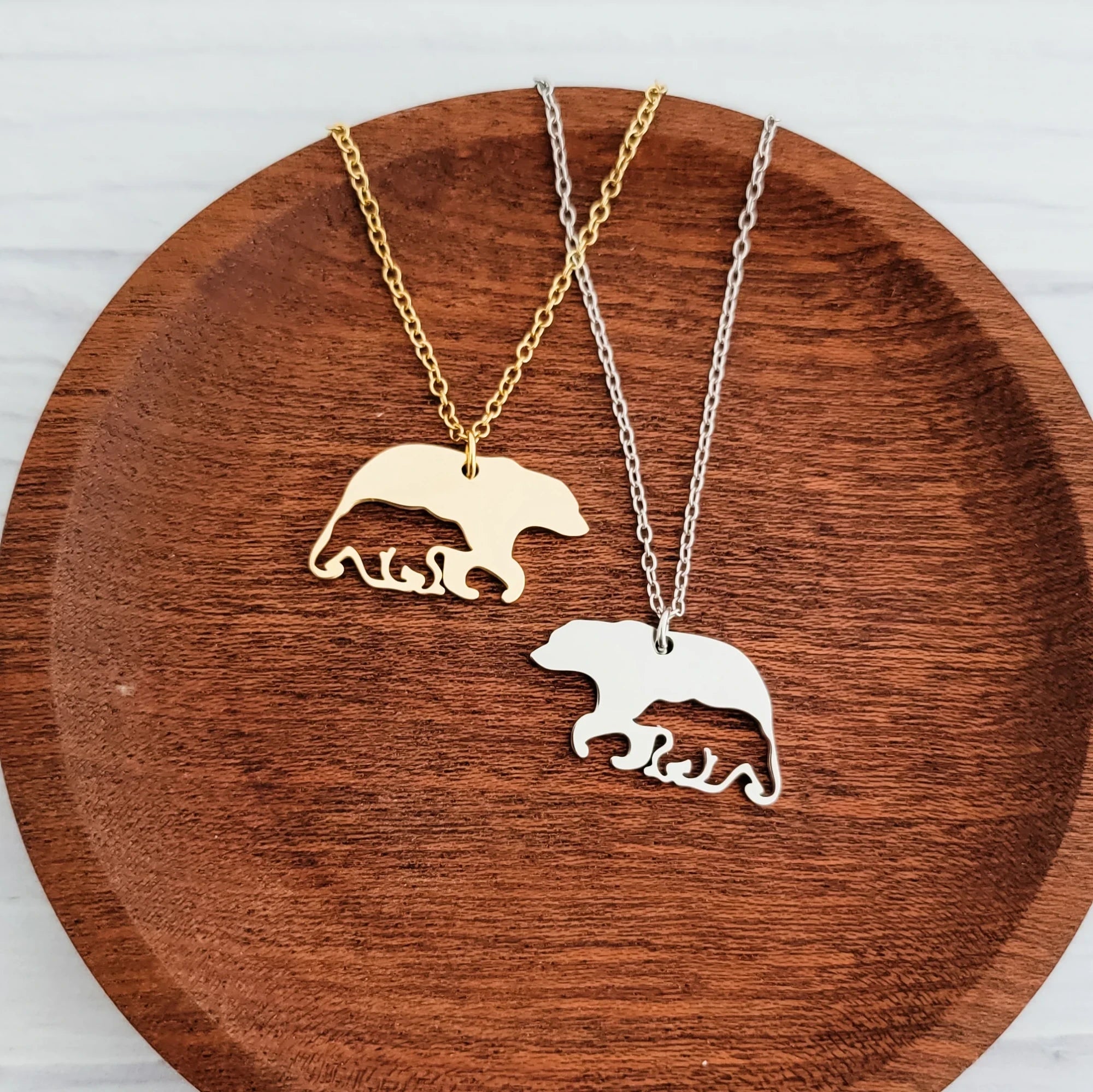 Roco Engraving gold and silver bear-and-cub stainless steel necklaces on a wooden tray