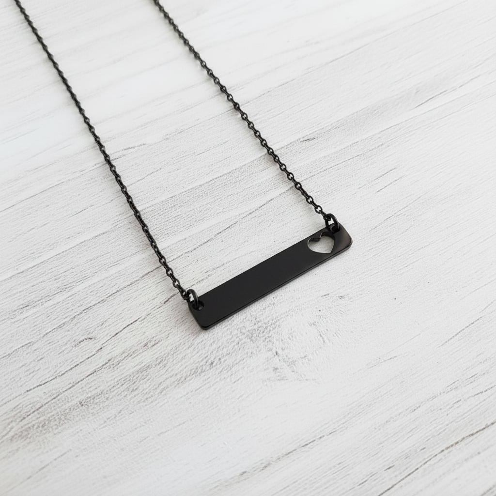 Roco Engraving black stainless steel horizontal bar necklace with a delicate heart cutout on a white wooden surface.
