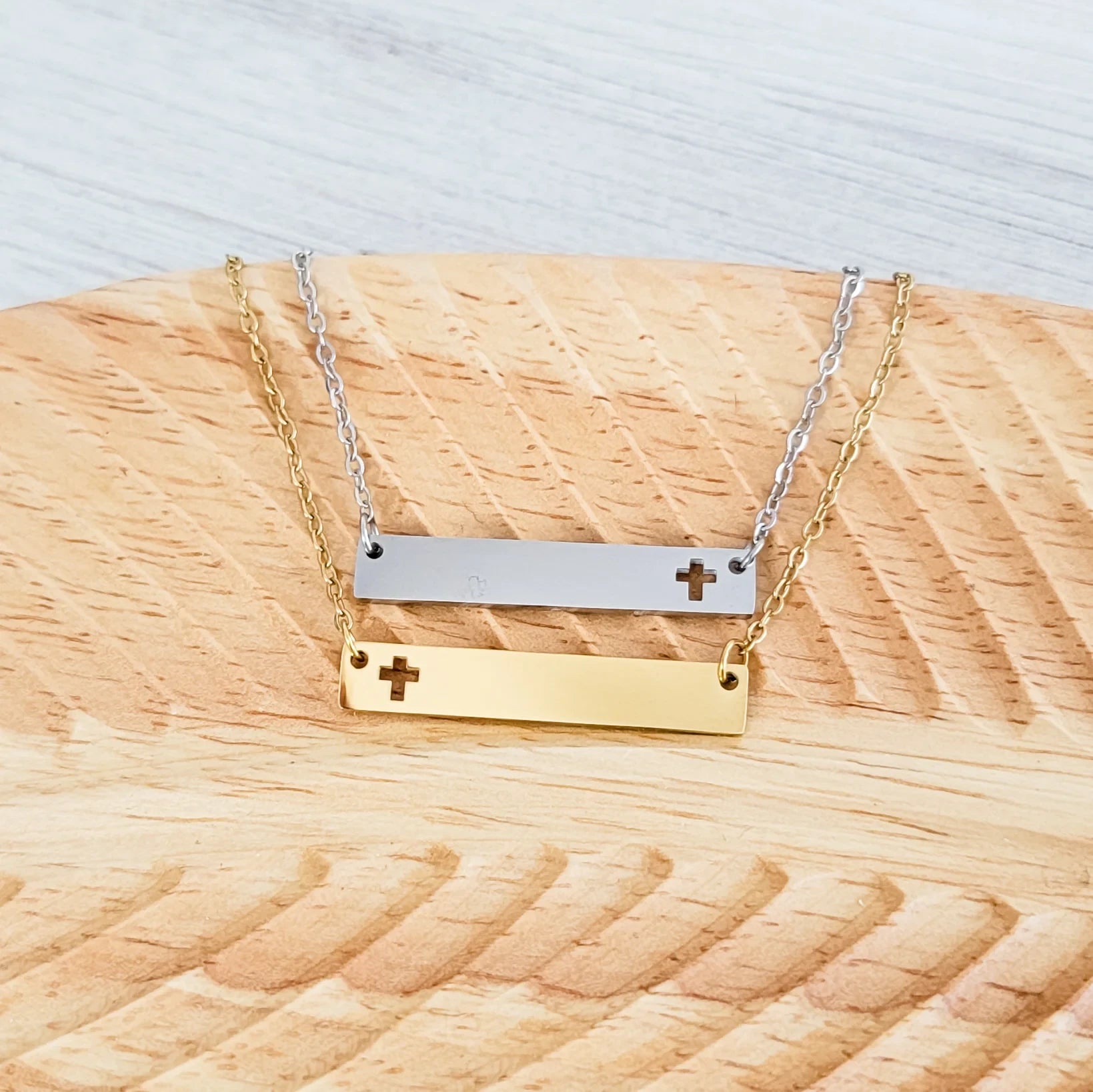 Roco Engraving silver and gold stainless steel bar necklaces with cross cutouts on a wooden display