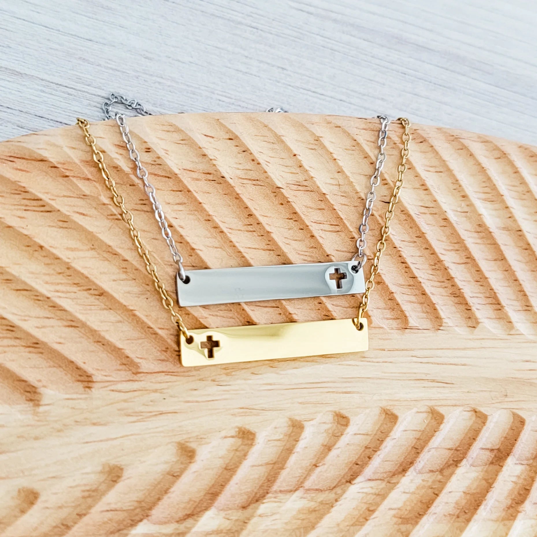 Roco Engraving silver and gold stainless steel cross bar necklaces with mirror finish on a wooden display