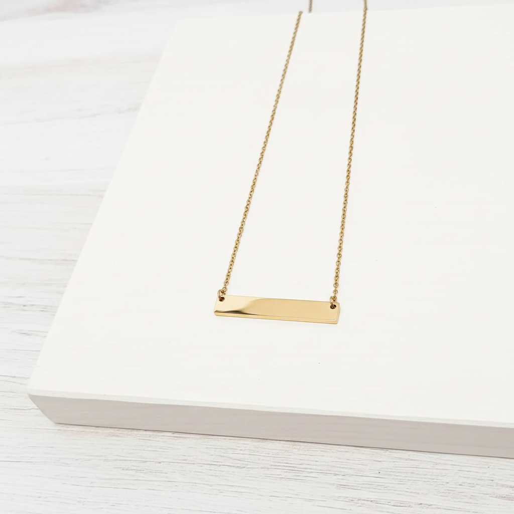 Roco Engraving gold bar necklace with a polished mirror finish on a white display stand