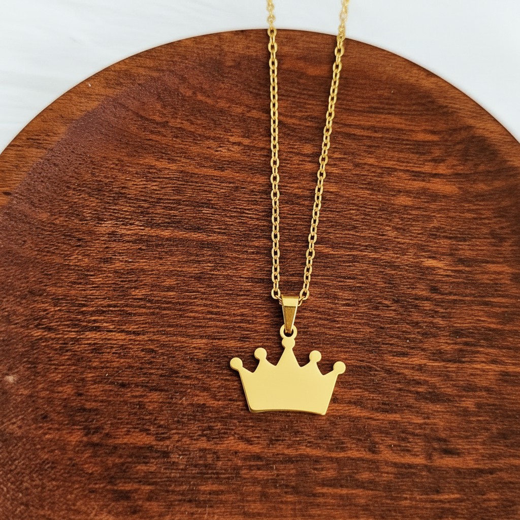 Roco Engraving gold crown pendant necklace on a polished wooden surface, featuring a delicate chain and mirror finish.