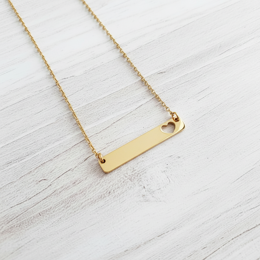 Roco Engraving gold bar necklace with a heart cutout on a delicate chain against a white wood background