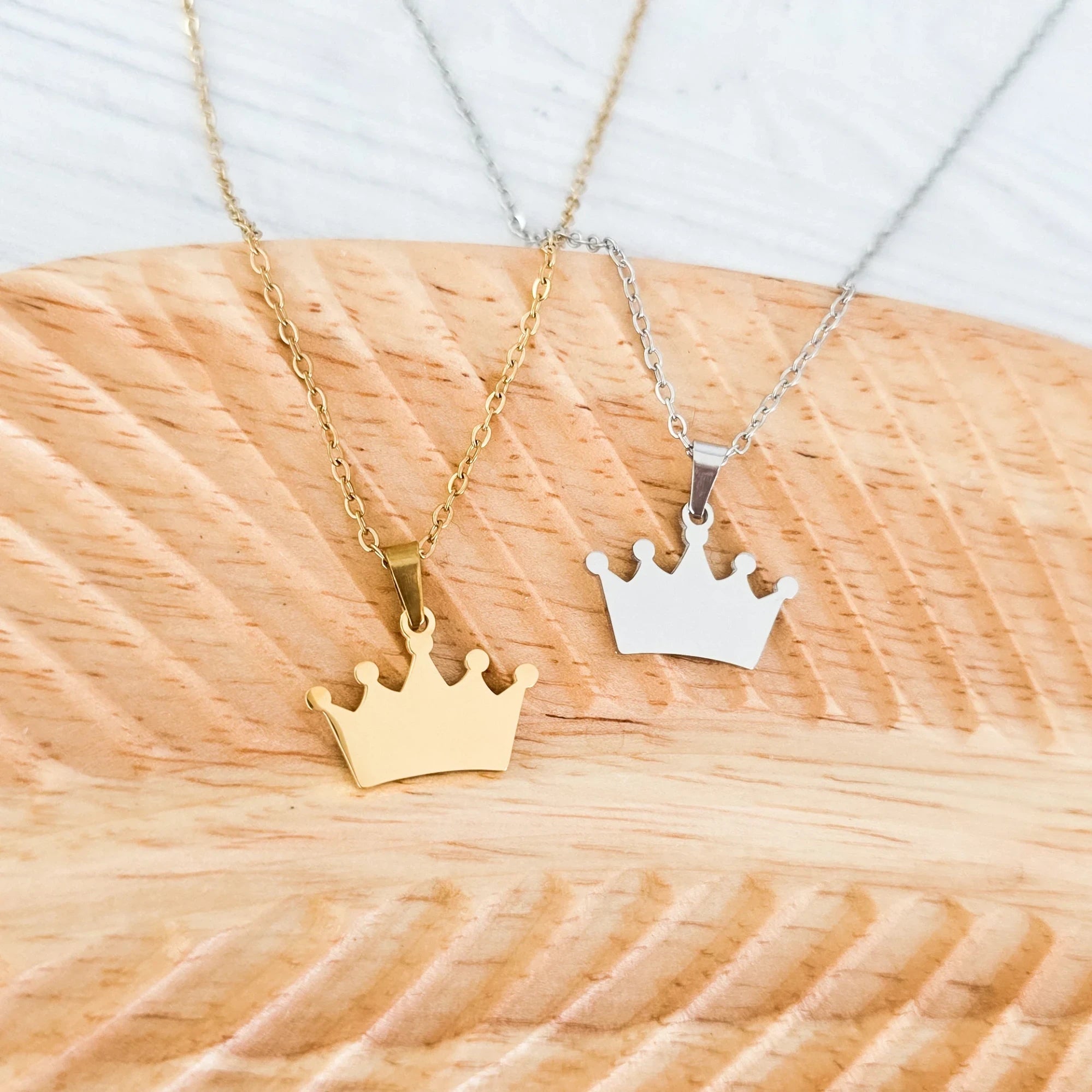 Roco Engraving gold and silver stainless steel crown pendant necklaces on a wooden display board