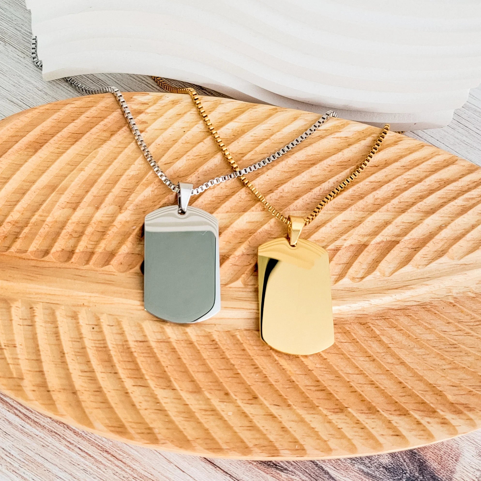 Roco Engraving silver and gold stainless steel dog tag necklaces on a wooden leaf-shaped display tray.