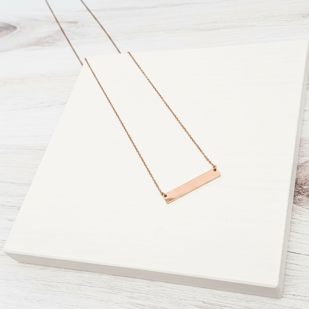Roco Engraving rose gold bar necklace with a polished mirror finish on a delicate chain displayed on a white block.