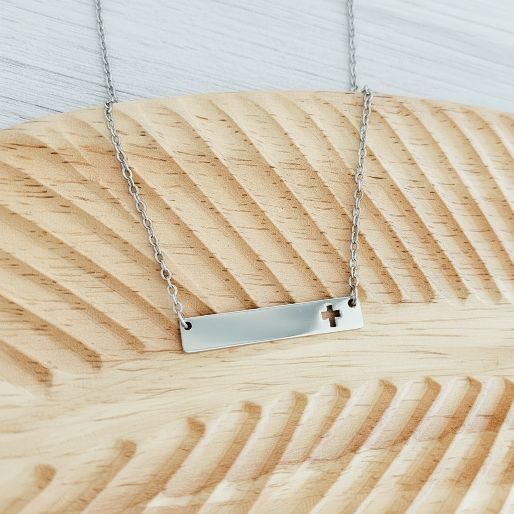 Roco Engraving silver stainless steel horizontal bar necklace with a cross cutout on a textured wooden background