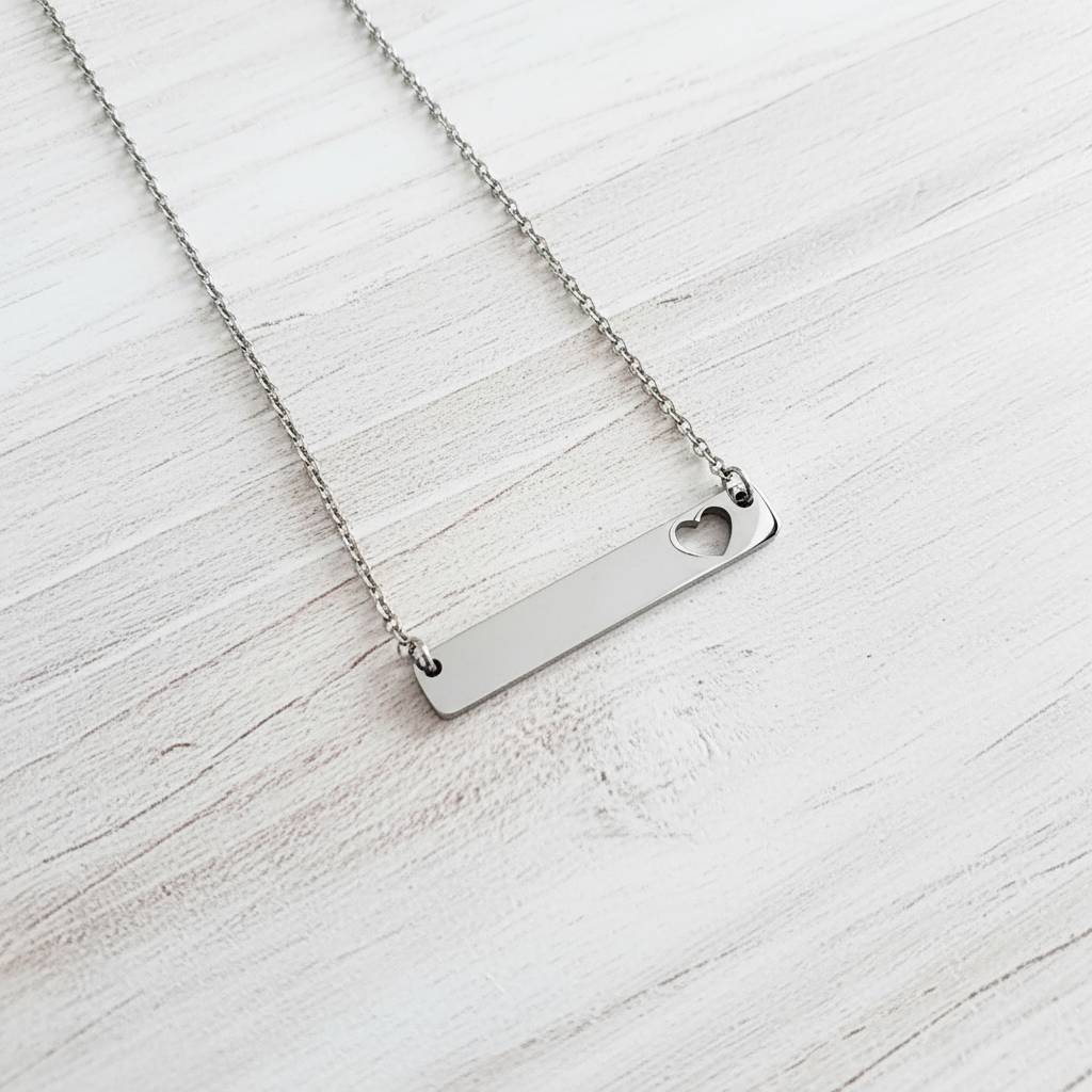 Roco Engraving silver stainless steel bar necklace with a delicate heart cutout on a white wooden background