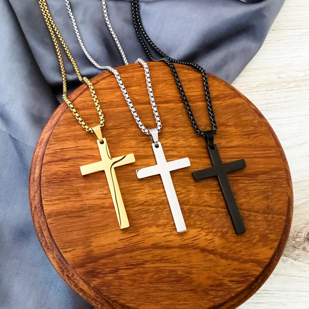 Roco Engraving gold, silver, and black stainless steel cross necklaces with box chains on a wooden display stand.