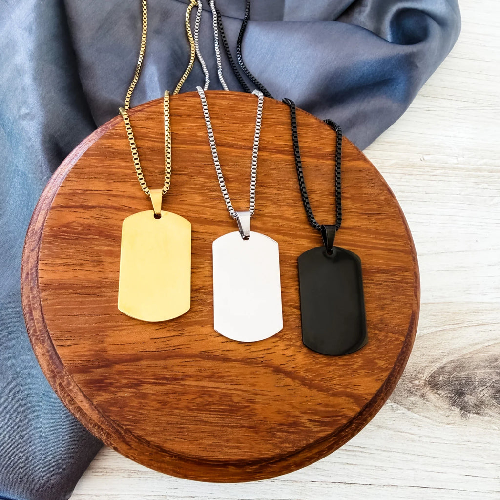 Roco Engraving custom dog tag necklaces in gold, silver, and black stainless steel on a wooden display stand.